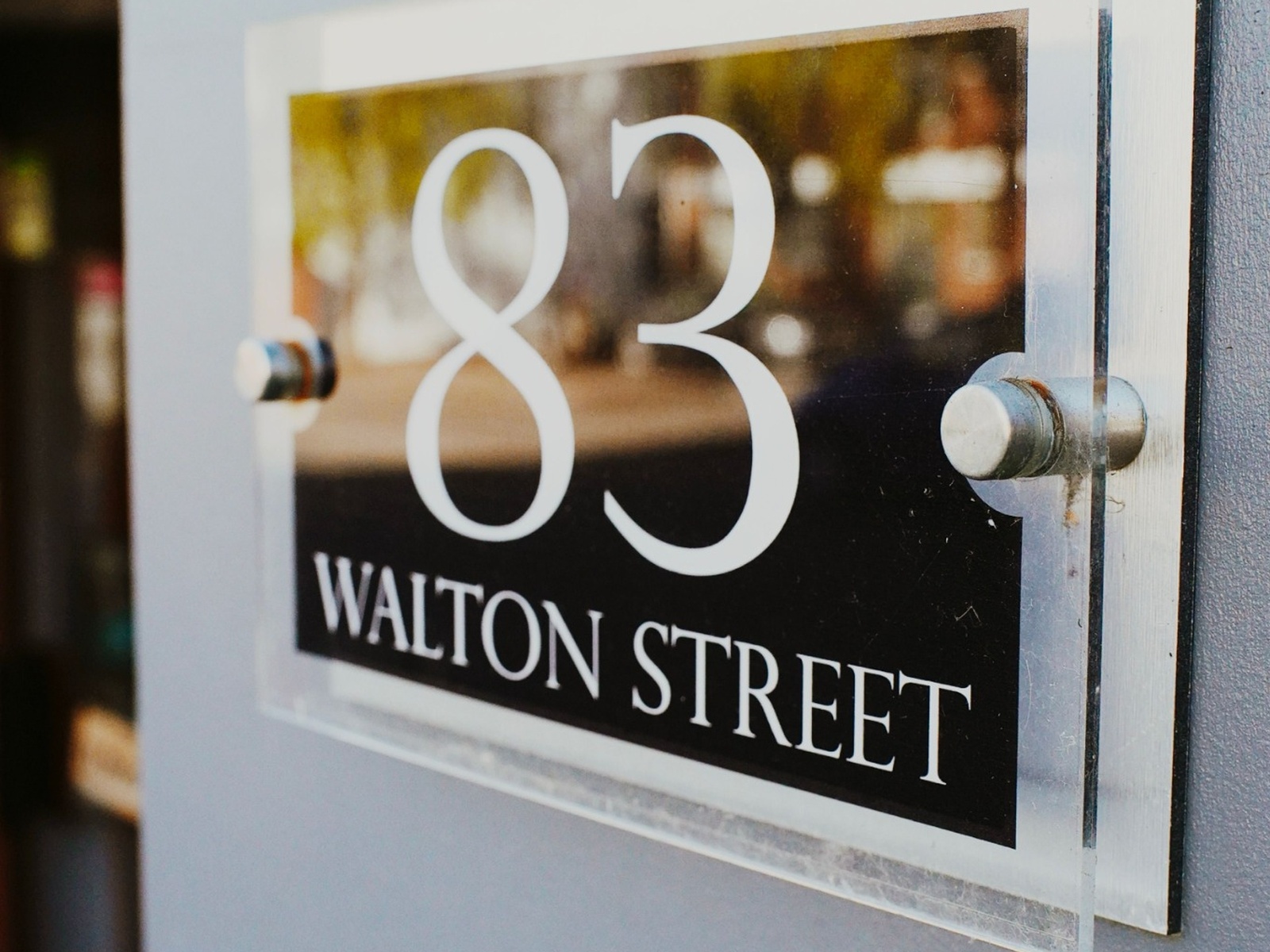 Wall-mounted clear acrylic sign face with polished edges and metal stand-off fixings.