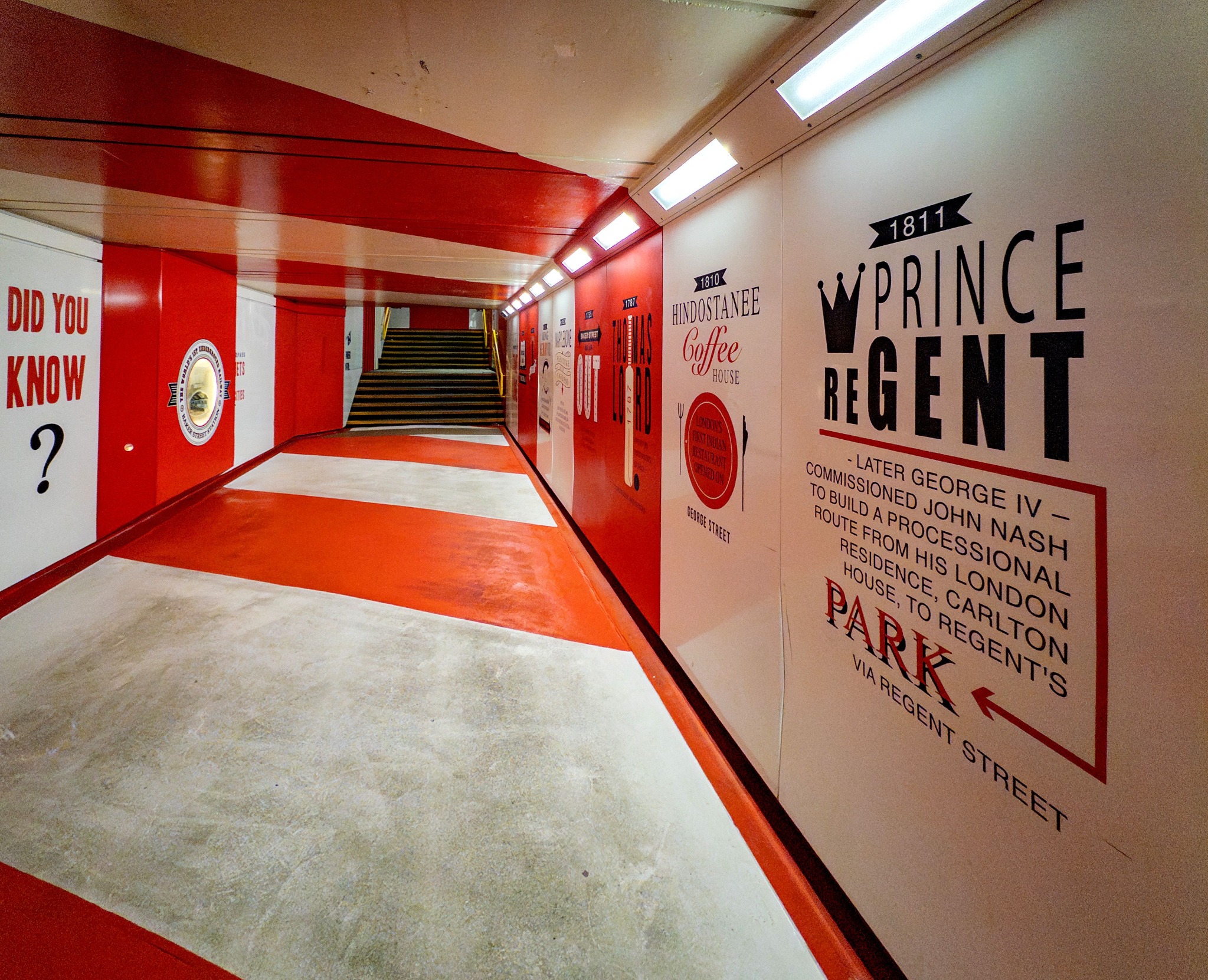 Large red and white branded graphic wall installation wrapping an exhibition corridor.