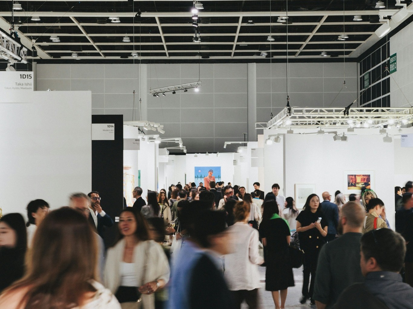 Wide view of a busy exhibition hall with visitors moving through branded stands and displays.