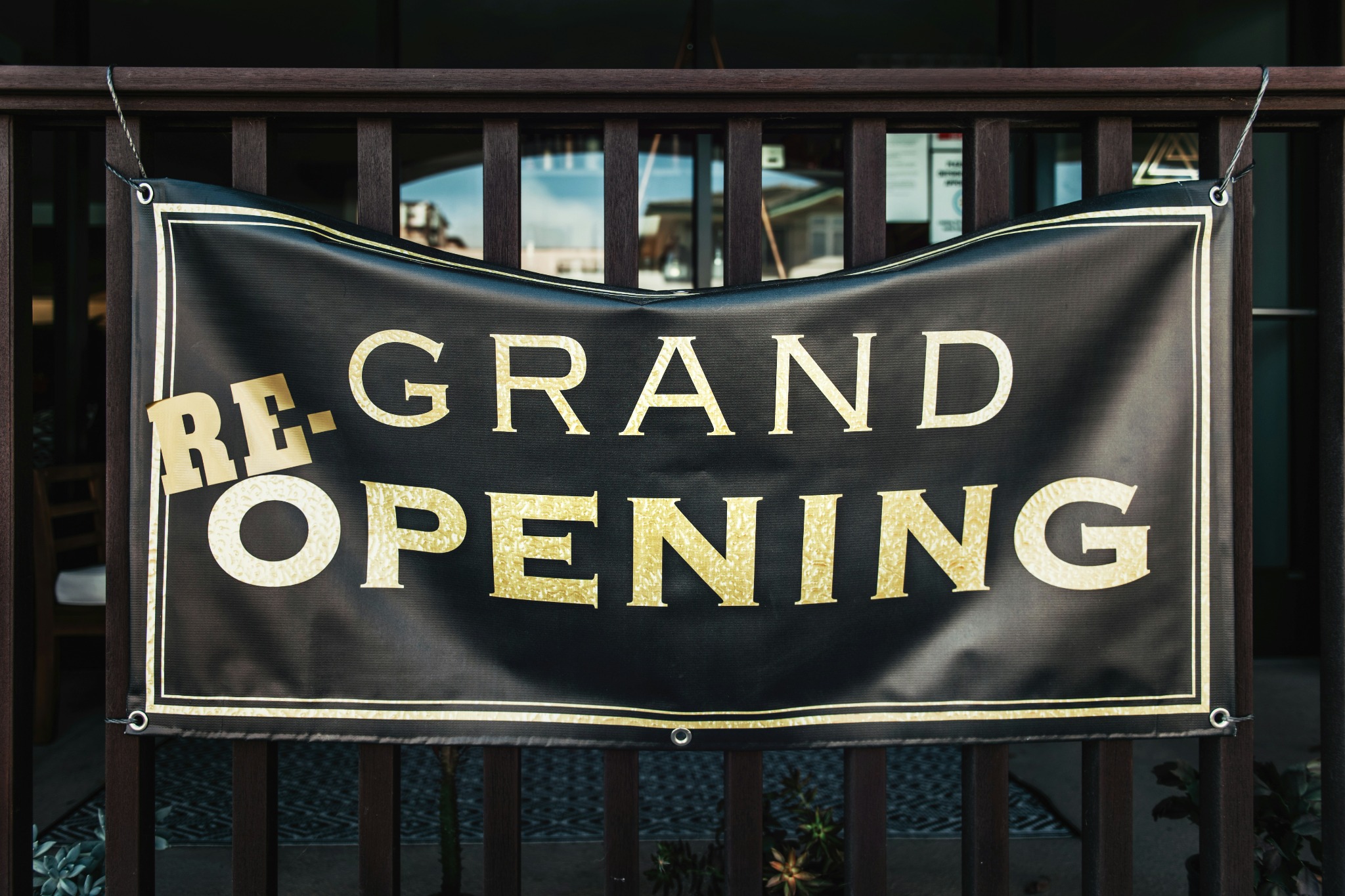 A large outdoor fabric reopening banner mounted to a timber railing, demonstrating soft signage.